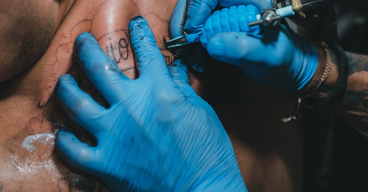 Traveling to Korea with special entry procedure because of COVID-19 - High angle hands of anonymous tattooist in blue gloves using professional tool to make tattoo on back of client in salon Traveling to Korea with special entry procedure because of COVID-19 - High angle hands of anonymous tattooist in blue gloves using professional tool to make tattoo on back of client in salon