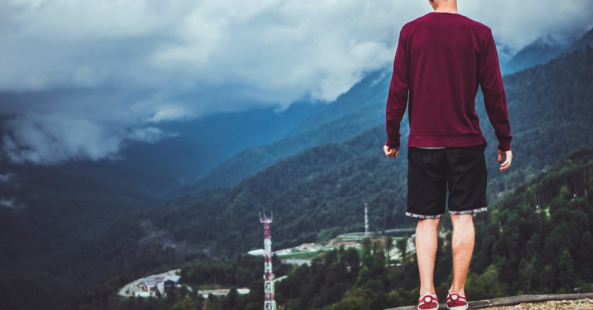 Traveling to the UK without adult supervision - Man Wearing Maroon Sweater and Black Shorts Standing in Front of Mountain Traveling to the UK without adult supervision - Man Wearing Maroon Sweater and Black Shorts Standing in Front of Mountain