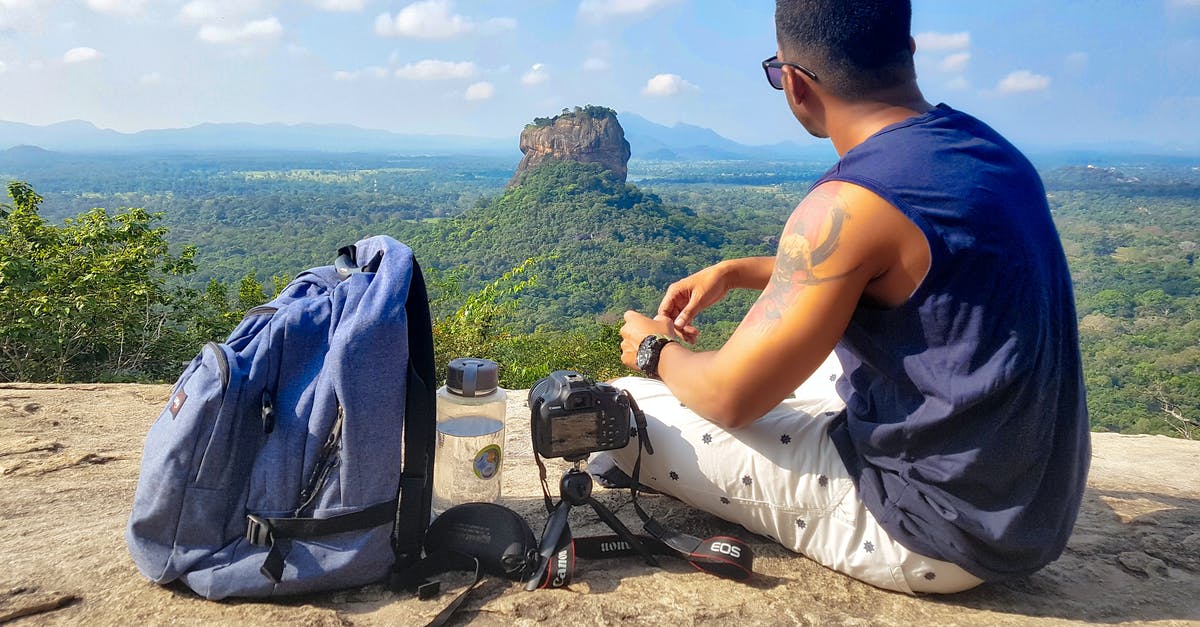 Traveling with BlackDiamond Jetforce avalanche rescue backpack - Man Sitting on Top of Gray Cliff Mountain Beside Backpack, Water Bottle, and Camera Traveling with BlackDiamond Jetforce avalanche rescue backpack - Man Sitting on Top of Gray Cliff Mountain Beside Backpack, Water Bottle, and Camera