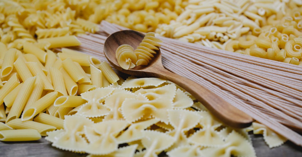 Travelling on Type D Schengen Italian visa - Arrangement of uncooked various pasta including spaghetti fusilli farfalle and penne heaped on table with wooden spoon