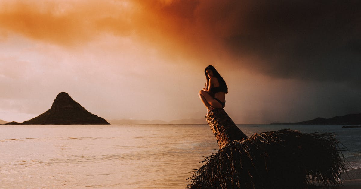 Travelling to Poland alone at the age of 17 - Full body side view of lonely female in swimwear sitting on old buoy near calm ocean against bright cloudy sky at sunset Travelling to Poland alone at the age of 17 - Full body side view of lonely female in swimwear sitting on old buoy near calm ocean against bright cloudy sky at sunset