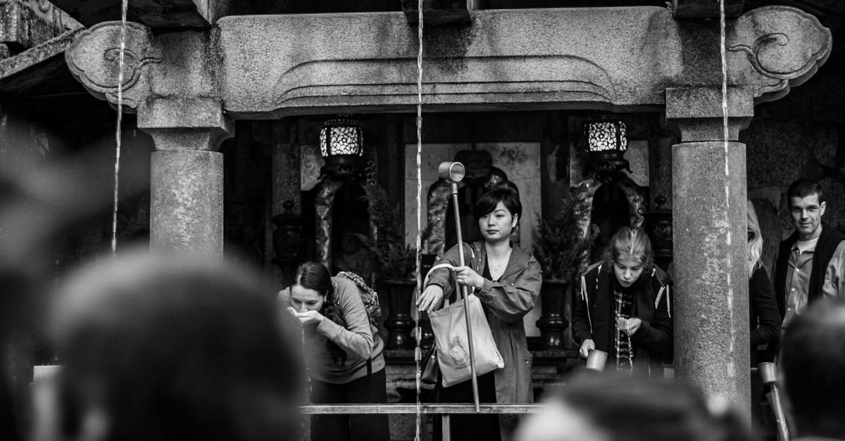 Travelling to the Sacred Well in Walsingham Norfolk (Sacred Spring in England) - Black and white of multiracial tourists drinking holy water while standing near old stone construction with narrow vertical pouring flows in sacred place Travelling to the Sacred Well in Walsingham Norfolk (Sacred Spring in England) - Black and white of multiracial tourists drinking holy water while standing near old stone construction with narrow vertical pouring flows in sacred place
