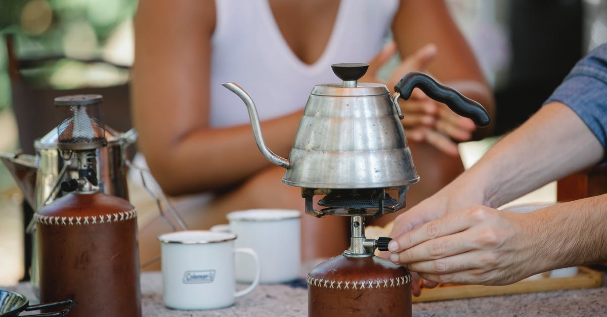 Travelling with a portable Stove and fuel canisters - Crop couple heating metal kettle on camp stove Travelling with a portable Stove and fuel canisters - Crop couple heating metal kettle on camp stove