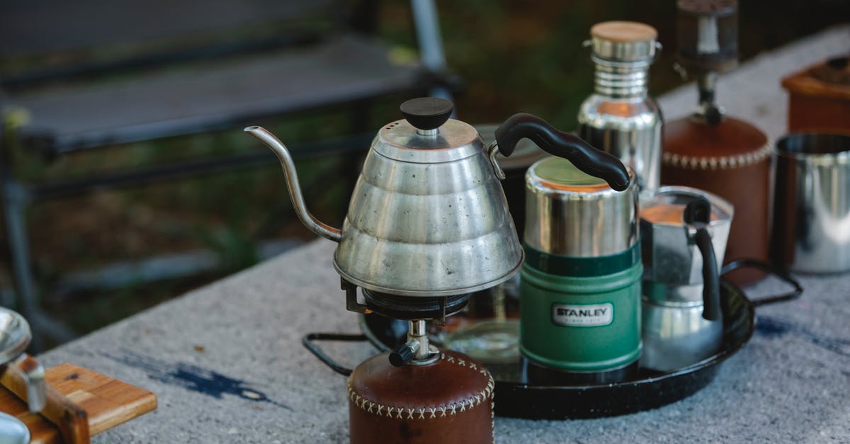 Travelling with a portable Stove and fuel canisters - High angle of metal coffee kettle placed on small portable camping gas stove near various utensils on table in nature Travelling with a portable Stove and fuel canisters - High angle of metal coffee kettle placed on small portable camping gas stove near various utensils on table in nature