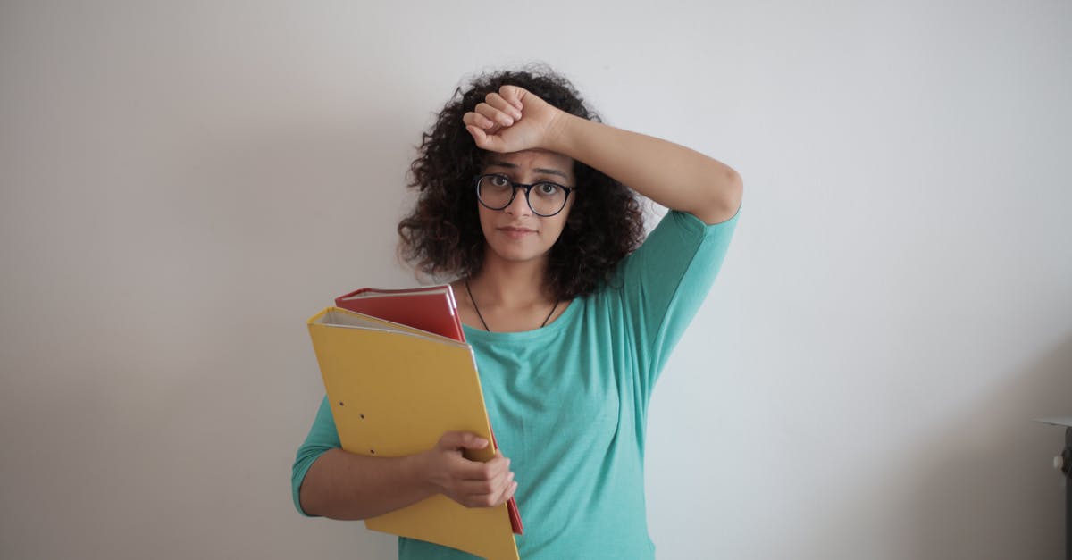 Trouble regarding Booking Tickets - Unhappy overworked female employee in glasses and casual clothes with folders of documents looking at camera with sadness and touching head while standing against white wall in contemporary office Trouble regarding Booking Tickets - Unhappy overworked female employee in glasses and casual clothes with folders of documents looking at camera with sadness and touching head while standing against white wall in contemporary office