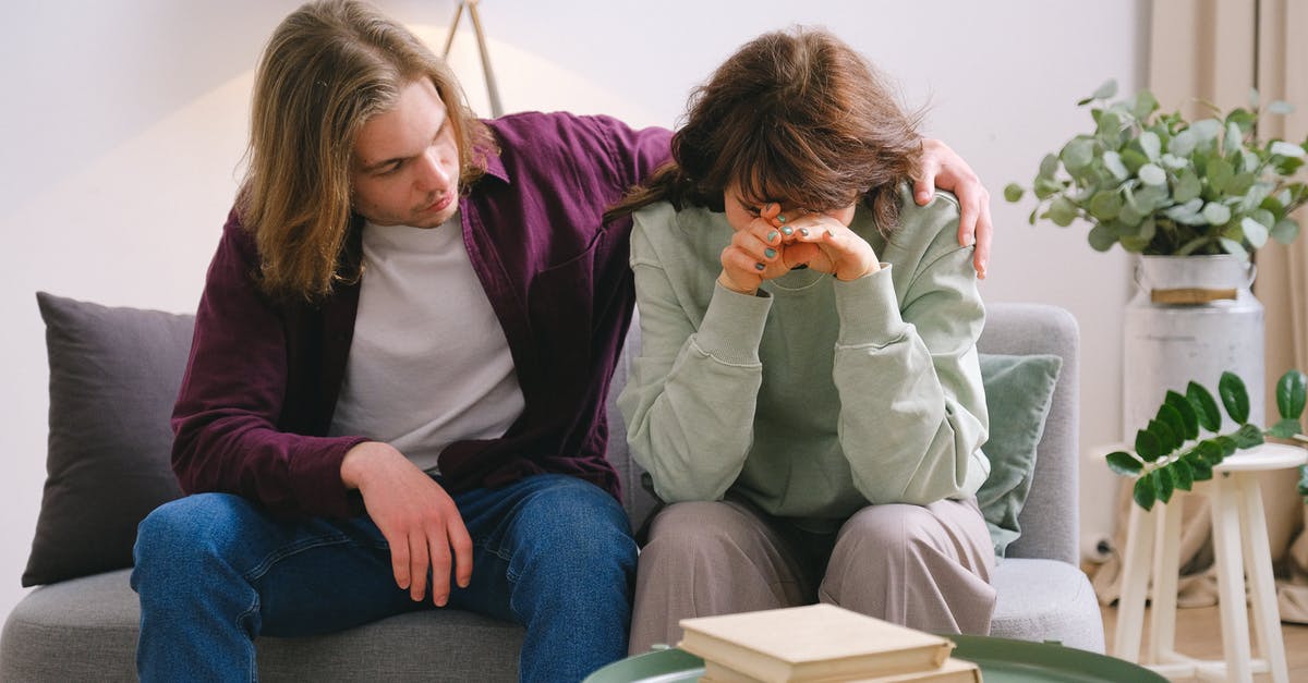 Trouble regarding Booking Tickets - Young male in jeans comforting depressed upset female crying on gray sofa near table with books Trouble regarding Booking Tickets - Young male in jeans comforting depressed upset female crying on gray sofa near table with books