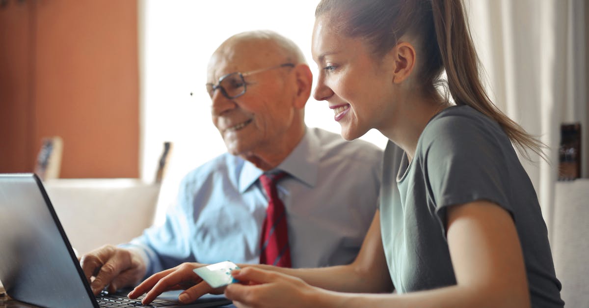 Uber and prepaid internet service - Young woman in casual clothes helping senior man in formal shirt with paying credit card in Internet using laptop while sitting at table Uber and prepaid internet service - Young woman in casual clothes helping senior man in formal shirt with paying credit card in Internet using laptop while sitting at table