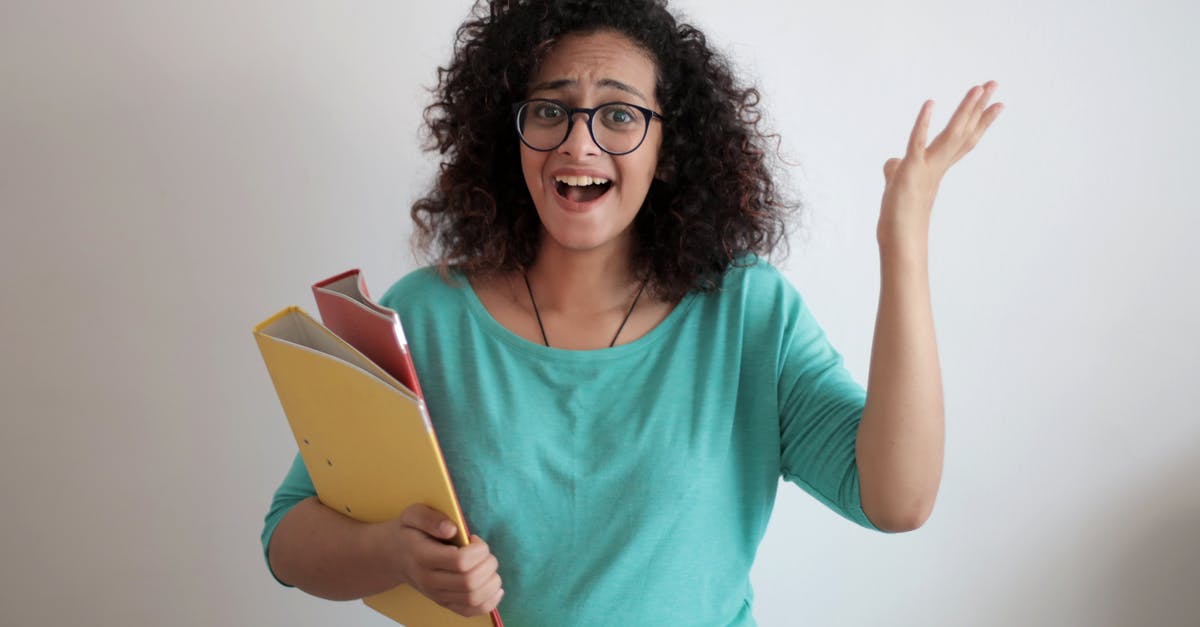 Uk business Visa checklist mistake - Dissatisfied annoyed woman with mouth opened wearing glasses and turquoise blouse looking away and screaming while standing against white wall with folders of documents and having problems in work