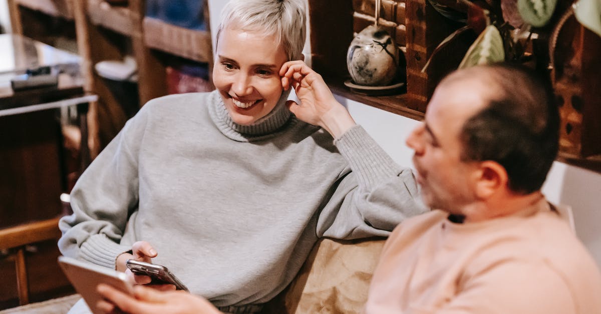 UK visitor visa for spouse - How to show proof of ties - From above of middle aged diverse in casual clothes smiling while sitting on sofa and using smartphone and tablet during weekend at home
