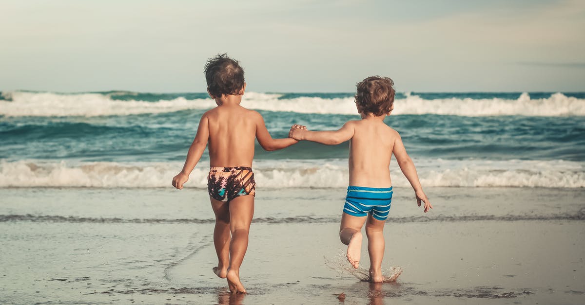 Uncrowded budget ski resort in the Alps with children which is also good to spend time for non-skiers - Back view of anonymous shirtless little brothers holding hands and walking on wet sandy beach towards waving ocean during summer holidays Uncrowded budget ski resort in the Alps with children which is also good to spend time for non-skiers - Back view of anonymous shirtless little brothers holding hands and walking on wet sandy beach towards waving ocean during summer holidays