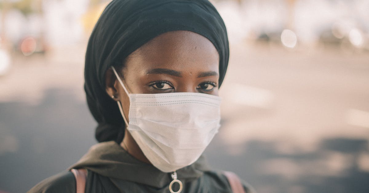 Under what situations might I be forced to quarantine while in the UK, if I am vaccinated outside the UK? - Unrecognizable young ethnic woman in jacket and headscarf and protective mask standing on city street