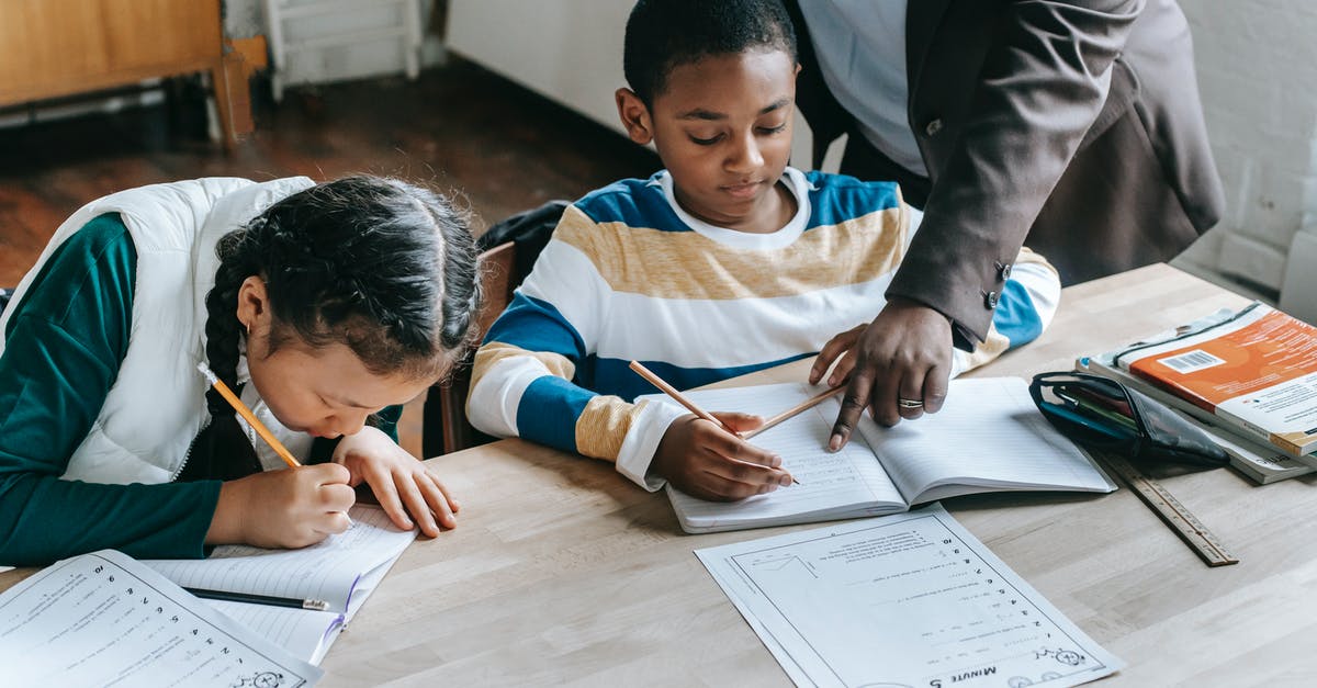 Unknown entry point for Schengen visa - High angle of crop unrecognizable black female teacher explaining task to focused little schoolboy sitting at desk near attentive Asian classmate writing in notebook Unknown entry point for Schengen visa - High angle of crop unrecognizable black female teacher explaining task to focused little schoolboy sitting at desk near attentive Asian classmate writing in notebook