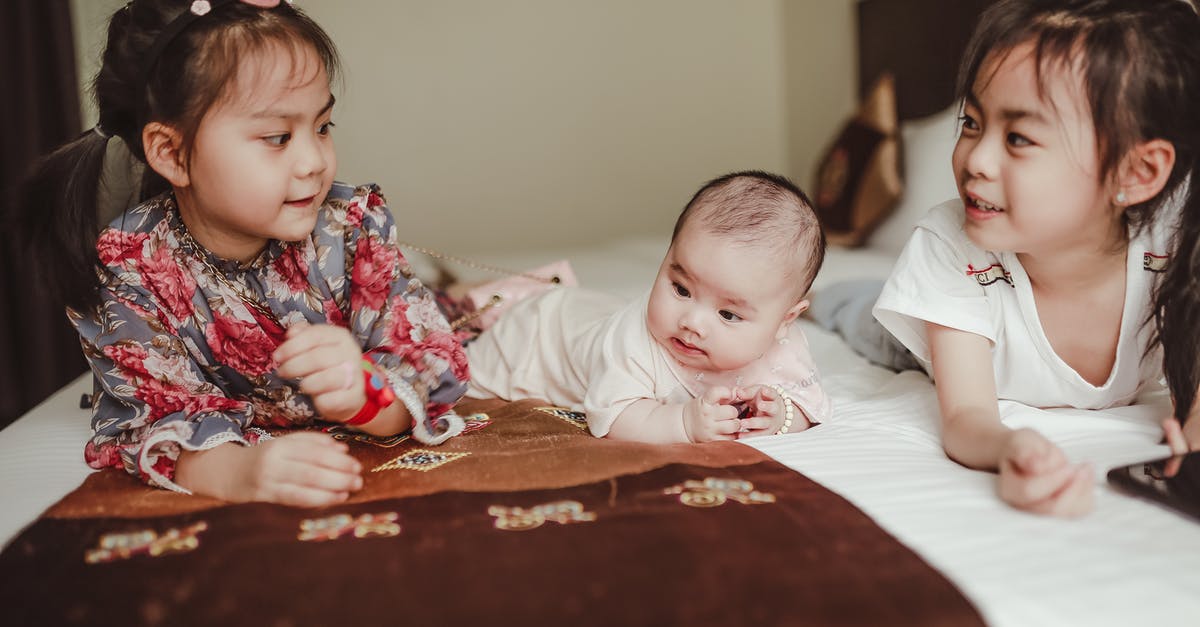US born but as a child of foreign diplomat - Cute little Asian girls and newborn baby lying on soft blanket on bed in light bedroom