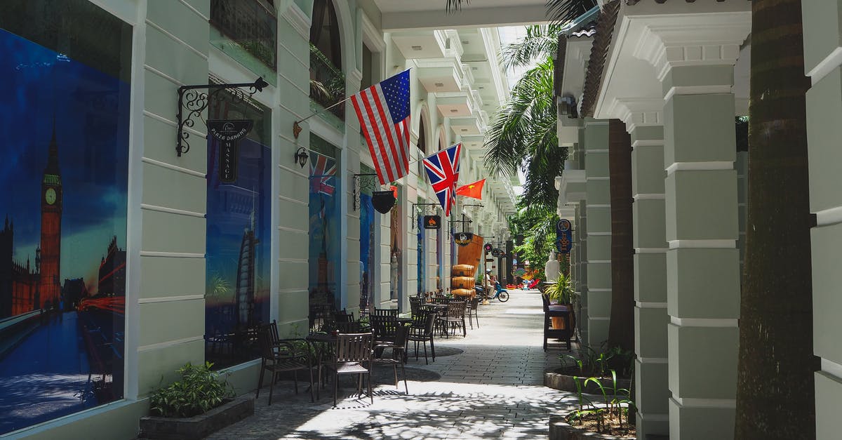 US citizen/HK resident travel documents need to go to mainland China - Narrow paved street with outdoor cafe and classic styled buildings decorated with various countries flags and banners in sunlight US citizen/HK resident travel documents need to go to mainland China - Narrow paved street with outdoor cafe and classic styled buildings decorated with various countries flags and banners in sunlight
