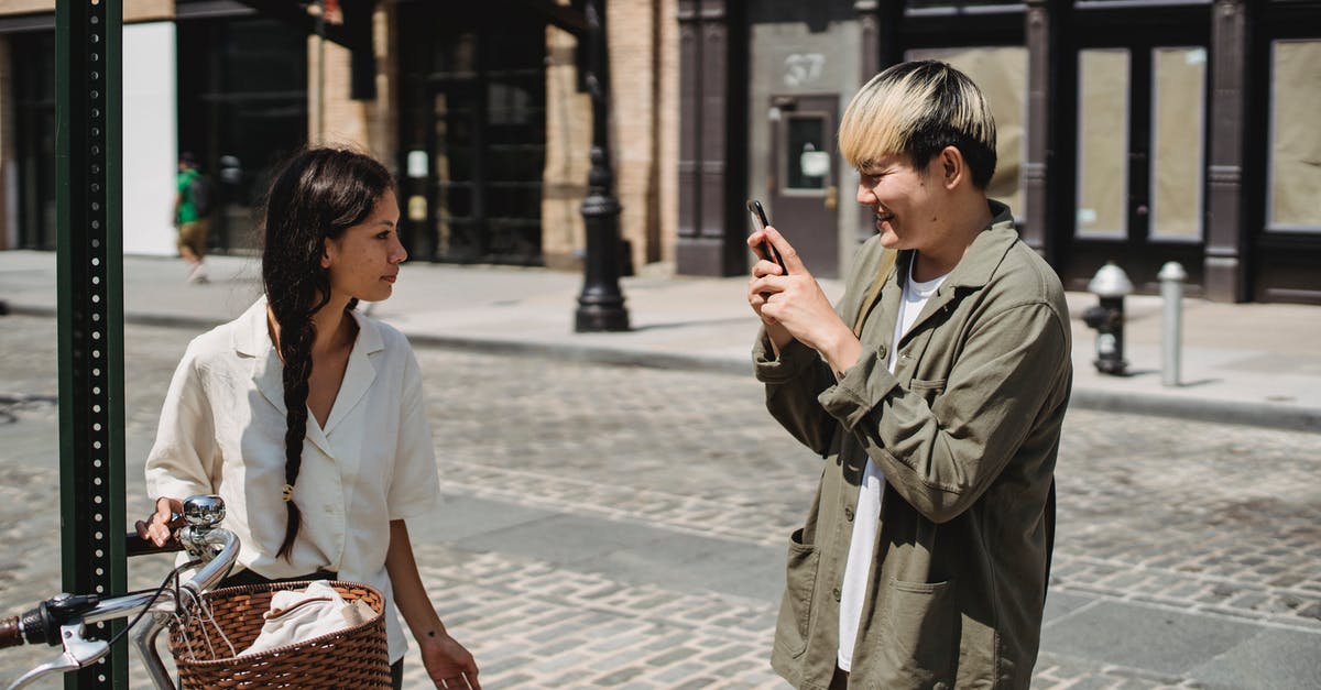 Use bike sharing service as a foreign tourist in China - Happy ethnic man taking photo of girlfriend standing on street near bicycle Use bike sharing service as a foreign tourist in China - Happy ethnic man taking photo of girlfriend standing on street near bicycle