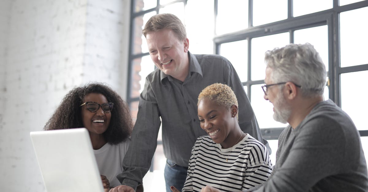 Using a Schengen type D visa for a short internship in a different country - Group of diverse people laughing and using netbook while working on project together in office with white brick walls and big window