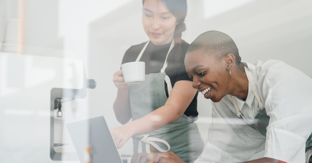 Using APC kiosk with new ESTA/passport - Through glass of friendly young Asian head barista showing young cheerful African American female coworker how to use special program on laptop Using APC kiosk with new ESTA/passport - Through glass of friendly young Asian head barista showing young cheerful African American female coworker how to use special program on laptop