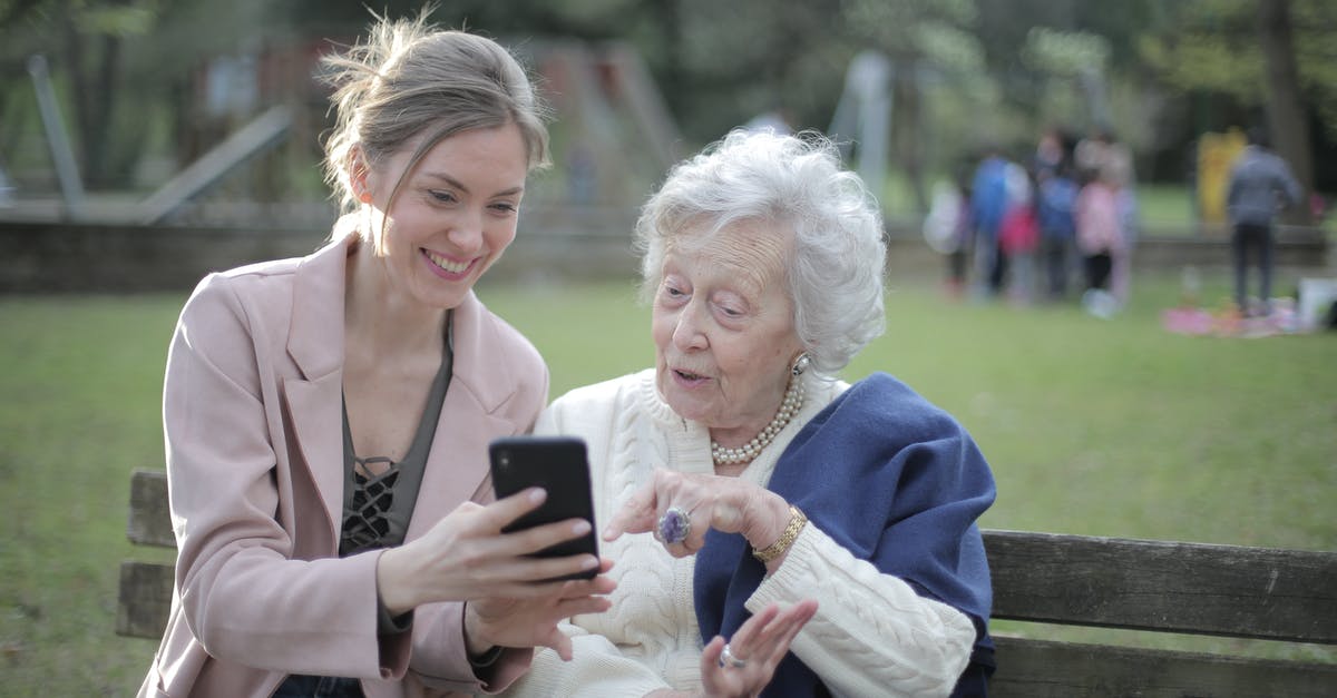 Using Australian mobile in China - Delighted female relatives sitting together on wooden bench in park and browsing mobile phone while learning using Using Australian mobile in China - Delighted female relatives sitting together on wooden bench in park and browsing mobile phone while learning using