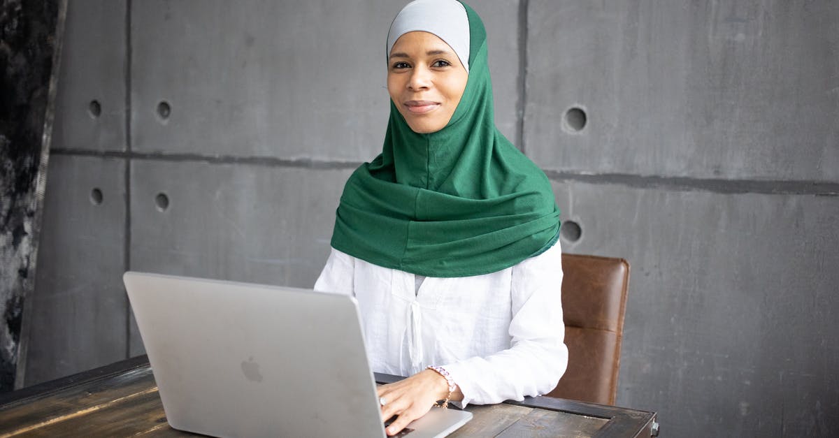 Using Modern Standard Arabic in Arabic-speaking countries - Positive Arab female freelancer using laptop while sitting at table Using Modern Standard Arabic in Arabic-speaking countries - Positive Arab female freelancer using laptop while sitting at table