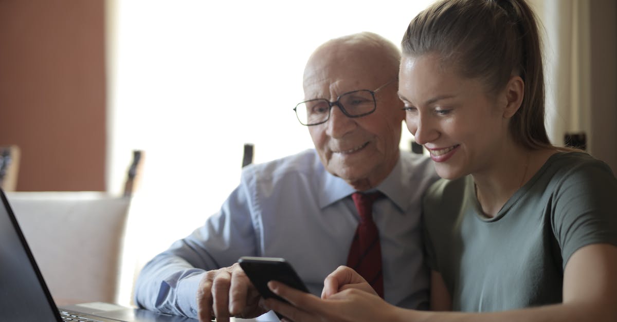 Using Multiple Entry Type C Visa for business meeting then tourism [closed] - Positive senior man in formal shirt and eyeglasses and smiling young granddaughter sharing mobile phone while sitting near laptop at table