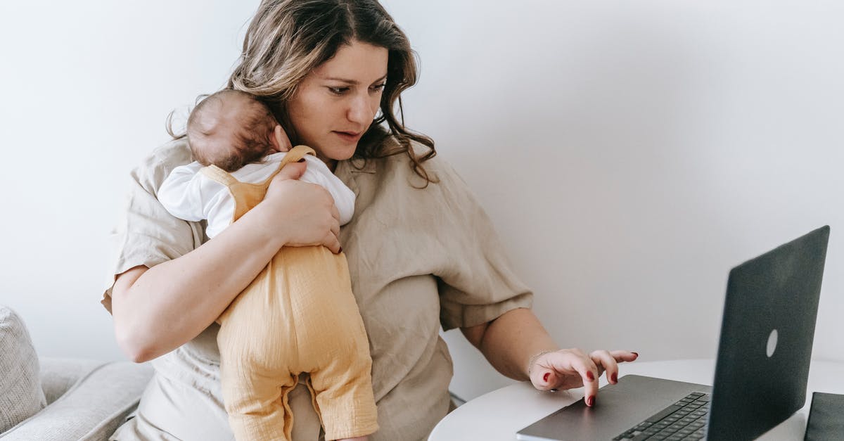 Using no-show ticket for infant - Concentrated young female freelancer embracing newborn while sitting at table and working remotely on laptop at home Using no-show ticket for infant - Concentrated young female freelancer embracing newborn while sitting at table and working remotely on laptop at home