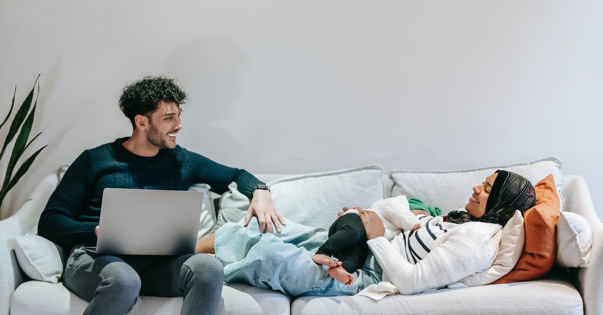 Using no-show ticket for infant - Cheerful young black Muslim woman in casual clothes and hijab relaxing on bed with cute infant in arms and communicating with ethnic husband working remotely on laptop Using no-show ticket for infant - Cheerful young black Muslim woman in casual clothes and hijab relaxing on bed with cute infant in arms and communicating with ethnic husband working remotely on laptop