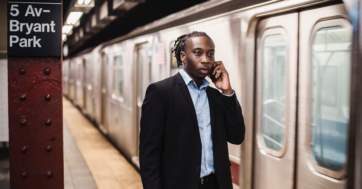 Using smartphone train ticket in Italy - Serious African American male in formal suit talking on smartphone while waiting for underground train to stop Using smartphone train ticket in Italy - Serious African American male in formal suit talking on smartphone while waiting for underground train to stop
