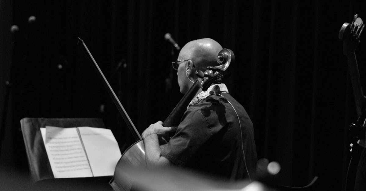 VAT Refund on Used Musical Instruments - Black and white back view of male musician in earphone with violoncello and bow against musical notation VAT Refund on Used Musical Instruments - Black and white back view of male musician in earphone with violoncello and bow against musical notation
