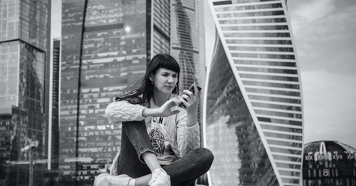 Visa requirements when connecting through Russia on separate tickets? - Black and white of young serious lady wearing casual outfit browsing smartphone while sitting on concrete fence against modern skyscrapers in Moscow Russia Visa requirements when connecting through Russia on separate tickets? - Black and white of young serious lady wearing casual outfit browsing smartphone while sitting on concrete fence against modern skyscrapers in Moscow Russia