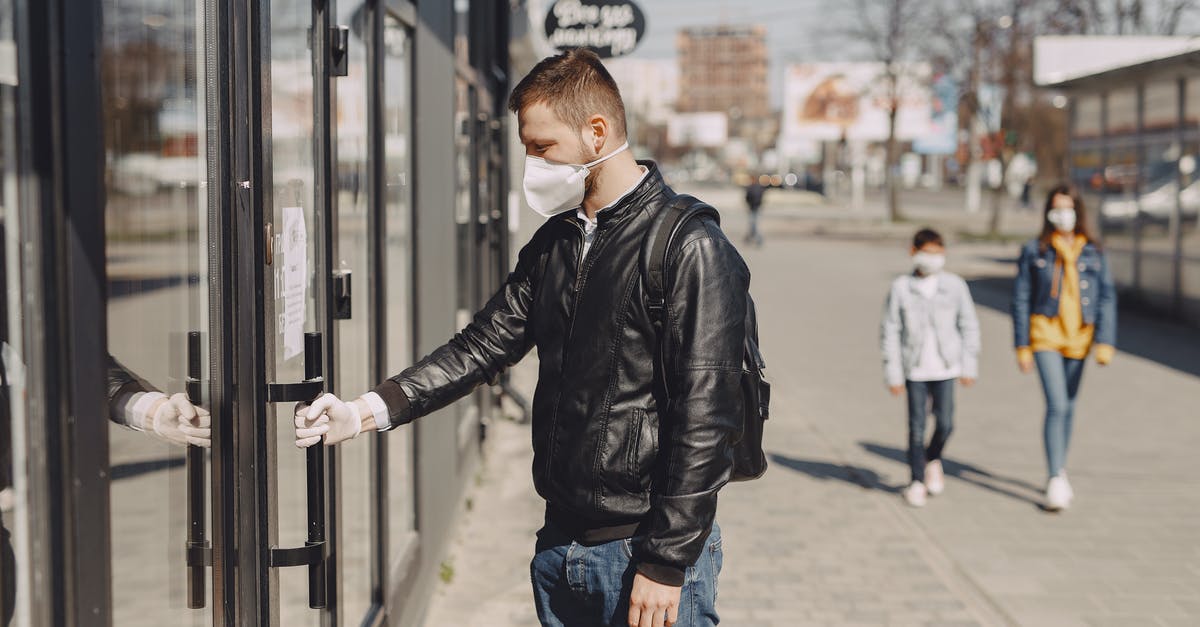 Visit Finland with visa issued from Norway during the COVID-19 outbreak - Side view of young guy in medical mask and disposable glove standing on sidewalk near shop and holding door handle while entering Visit Finland with visa issued from Norway during the COVID-19 outbreak - Side view of young guy in medical mask and disposable glove standing on sidewalk near shop and holding door handle while entering