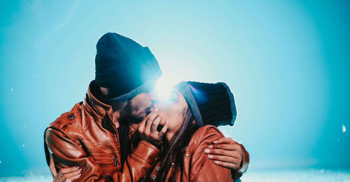 We are twins with different places of birth mentioned in the passport with the same date - Ethnic couple in same clothes cuddling and kissing near snow under bright blue sky in sunny weather in back lit