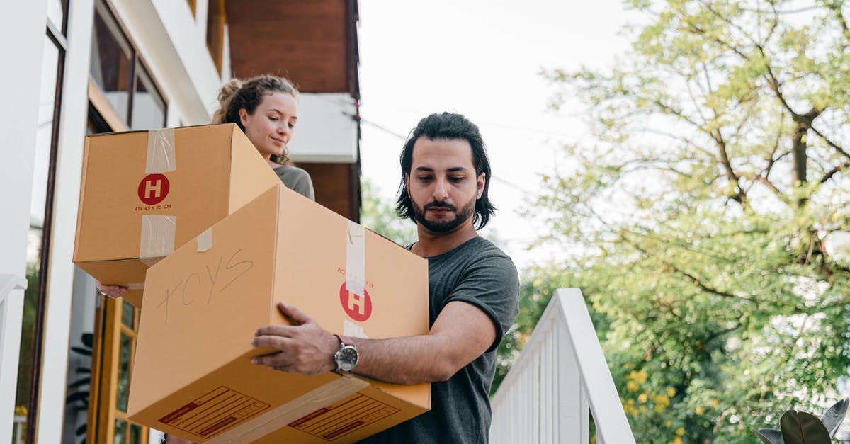 What action is recommended if your accommodation refuses to let you leave without paying additional fees? - Young multiracial boyfriend and girlfriend in casual wear carrying big carton boxes and watching step on porch stairs while moving out of old home on sunny day in summer