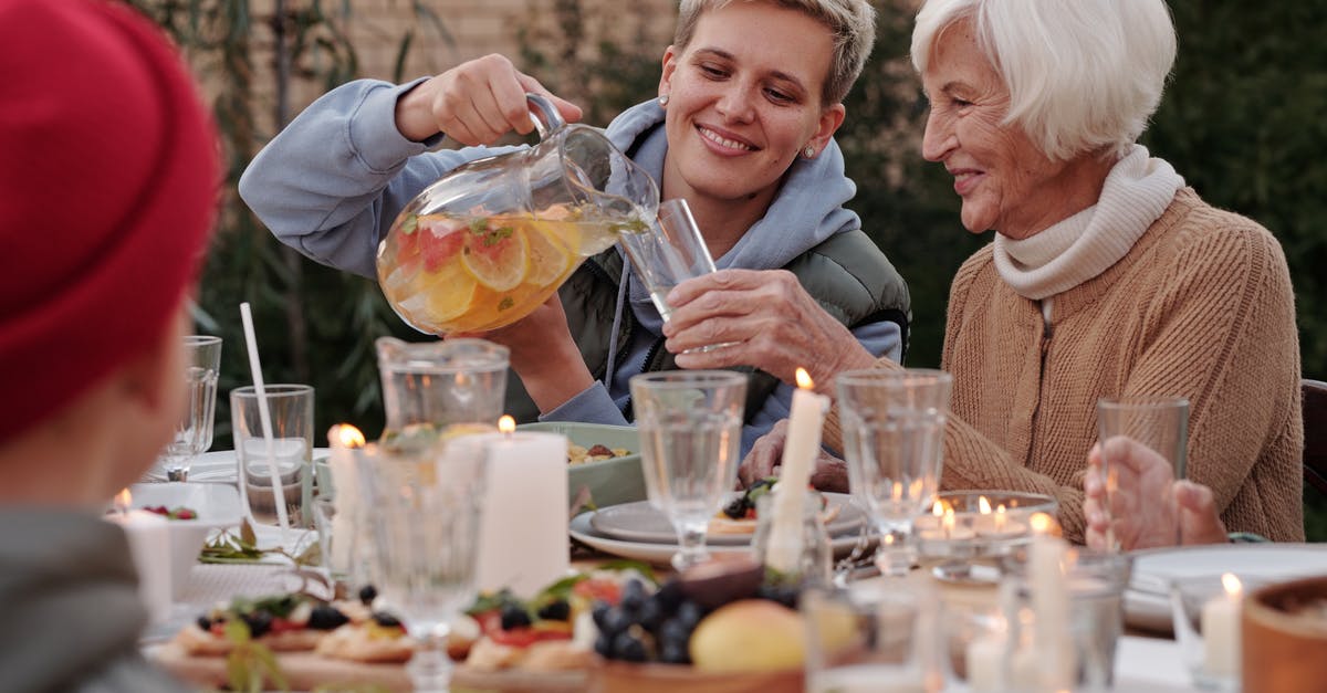 What are the candles outside in Denmark about? - Positive lady pouring drink into glass for elderly woman while having dinner with family on terrace What are the candles outside in Denmark about? - Positive lady pouring drink into glass for elderly woman while having dinner with family on terrace