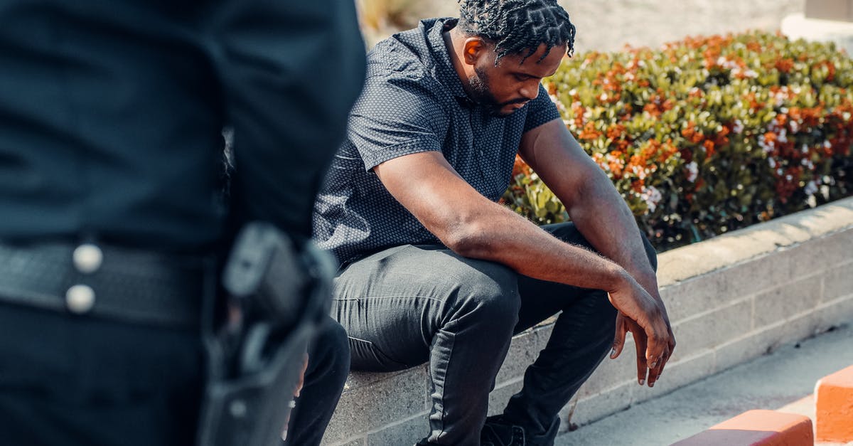 What can security officials do when they suspect my checked baggage? - Man in Gray Button Up Shirt and Gray Denim Jeans Sitting on Concrete Block Beside a Police Officer