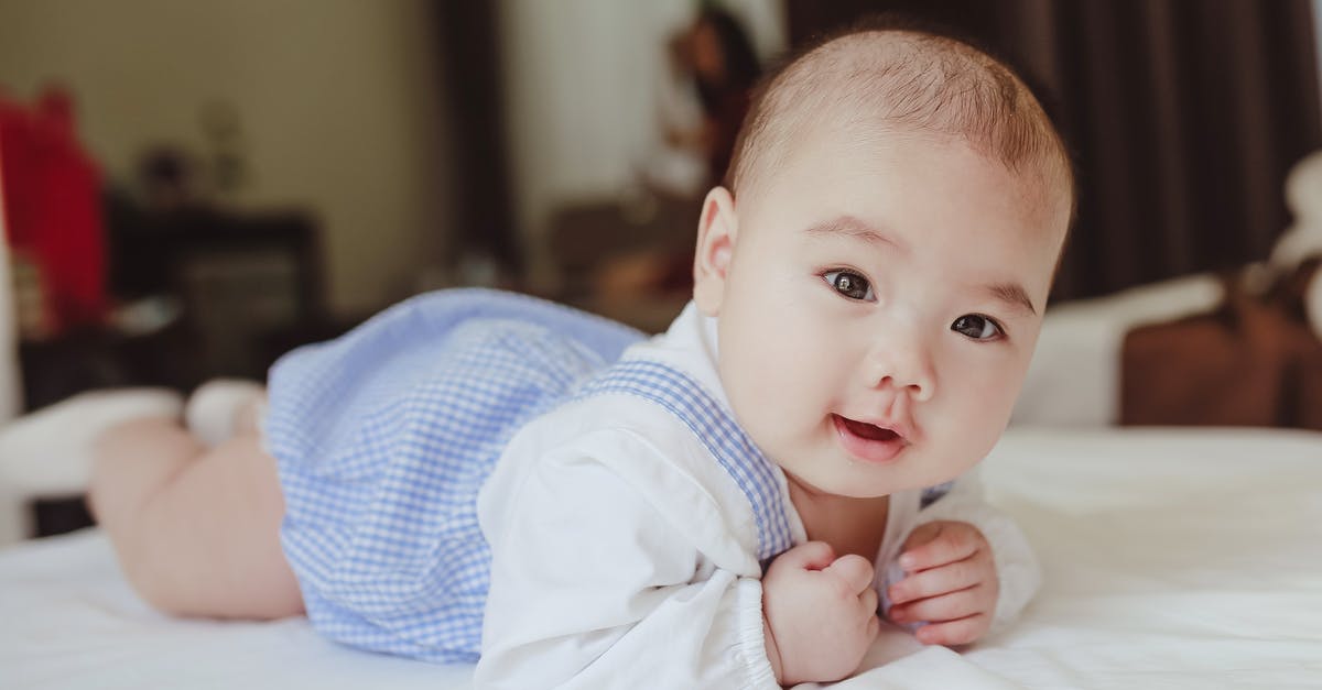 What citizenship/place of birth would a child born on an airplane have? - Adorable newborn baby in white cotton shirt and blue bodysuit lying on bed in light room