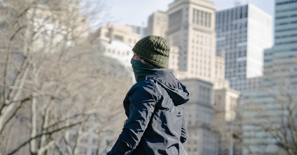 What city are these buildings in? - Person in Black Jacket and Green Knit Cap in the Park What city are these buildings in? - Person in Black Jacket and Green Knit Cap in the Park