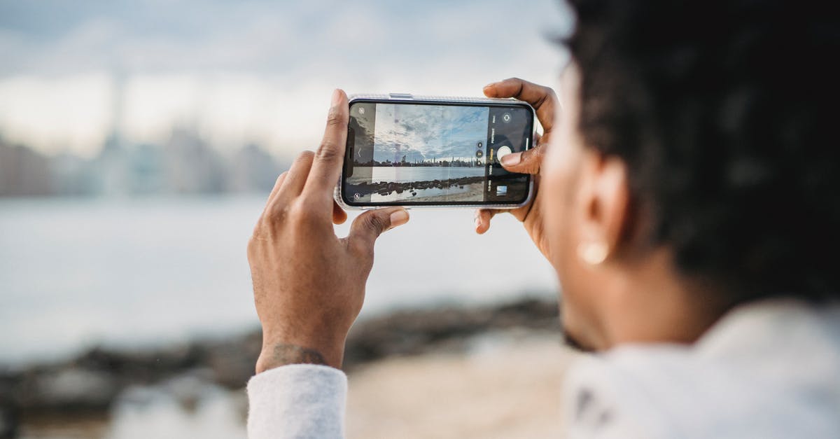 What coast or river-adjacent city is in this photo? - Back view of crop African American male taking picture on mobile phone of coastal city located on river bank What coast or river-adjacent city is in this photo? - Back view of crop African American male taking picture on mobile phone of coastal city located on river bank