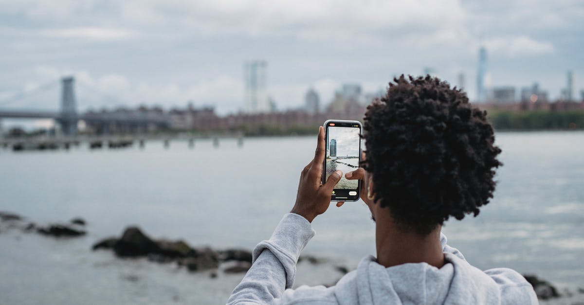 What coast or river-adjacent city is in this photo? - Black man taking photo of bridge on smartphone What coast or river-adjacent city is in this photo? - Black man taking photo of bridge on smartphone