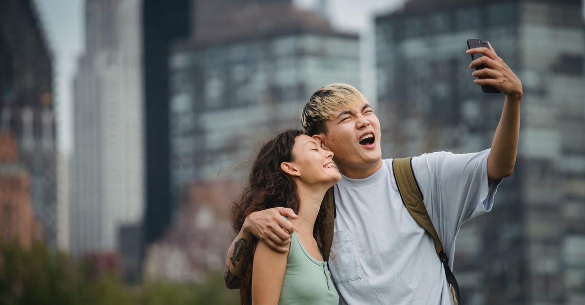 What do I need to have for 12 hours stopover with a small trip to Kiev city? [closed] - Cheerful young ethnic couple hugging and making face while standing in park near modern skyscrapers and taking selfie on smartphone