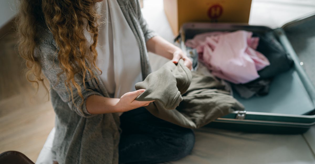 What do I need to prepare for if I am making a trip out of state from New York? - From above crop anonymous female in casual wear sitting on bed and packing luggage while preparing to move out What do I need to prepare for if I am making a trip out of state from New York? - From above crop anonymous female in casual wear sitting on bed and packing luggage while preparing to move out