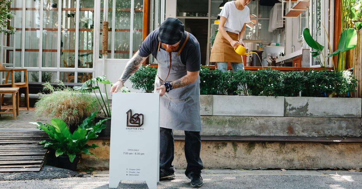 What do I put here? - Couple of coworkers in aprons and casual clothes watering plants and putting signboard near cafeteria in daytime What do I put here? - Couple of coworkers in aprons and casual clothes watering plants and putting signboard near cafeteria in daytime