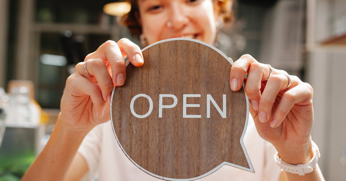 What do shops mean when they are open 7/7? - Happy young woman worker in casual clothes standing in light cafe and showing small sign with word open What do shops mean when they are open 7/7? - Happy young woman worker in casual clothes standing in light cafe and showing small sign with word open