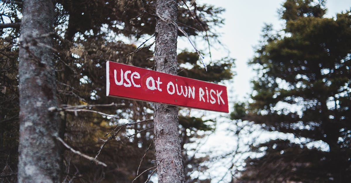 What does this sign on a hiking trail communicate? [closed] - From below of red sign with use at own risk text on tree trunk in autumn forest
