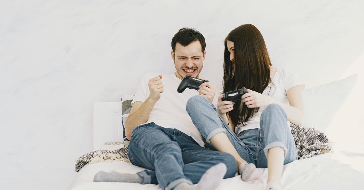 What games can I play with friends in the confined space of the seating on a long flight? [closed] - Happy man in white t shirt and jeans with closed eyes and game pad showing yes gesture after winning and lying on bed near girlfriend at home