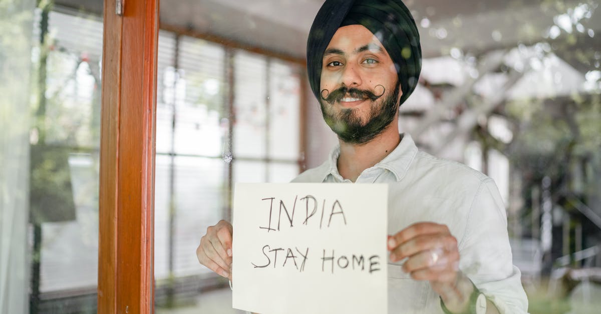 What happens if I test Covid positive while staying in a German Hotel - Indian man showing INDIA STAY HOME inscription through glass