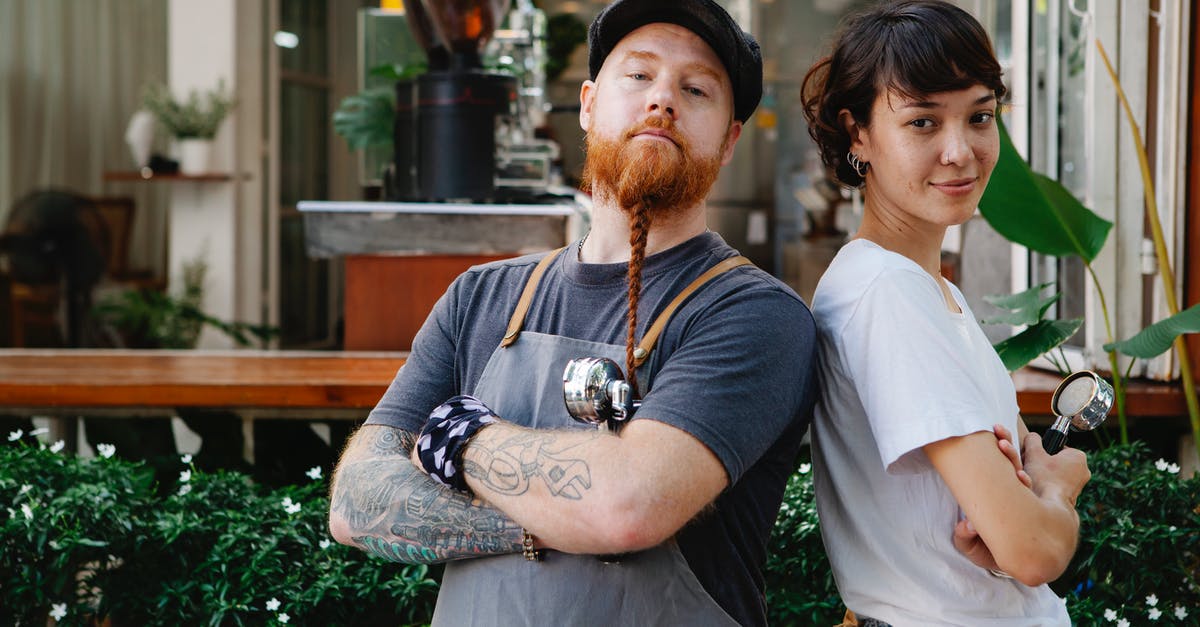 What happens if you don't register your local address when visiting Germany? - Couple of confident barista coworkers in aprons and casual outfit standing in street near cafeteria with portafilter near plants while looking at camera in daylight