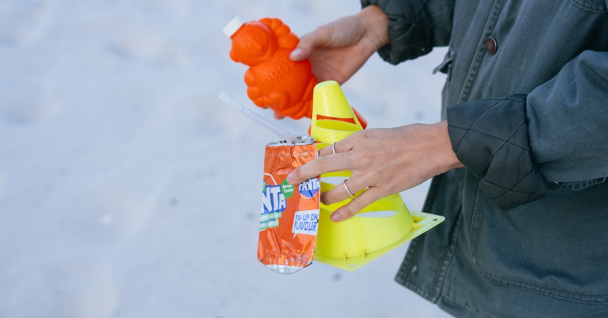 What happens to the garbage from a pre-customs side of an international airport? - From above side view of crop female activist in warm jacket holding plastic garbage collected on sandy beach
