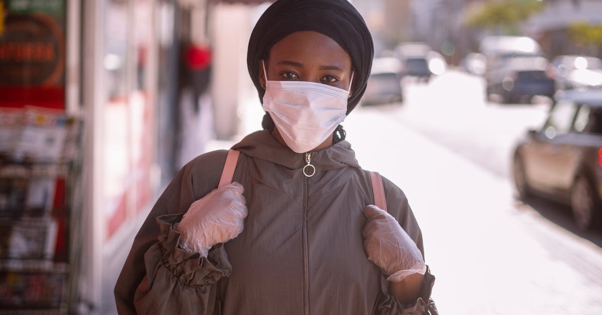 What happens when a town is under quarantine and my visa expires - Unrecognizable black female in outerwear and headscarf and protective mask and gloves standing on sidewalk of city street What happens when a town is under quarantine and my visa expires - Unrecognizable black female in outerwear and headscarf and protective mask and gloves standing on sidewalk of city street