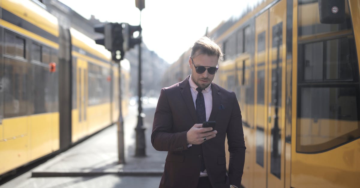 What is a copy of a valid state ID? Bus system application - Brutal male entrepreneur in elegant suit and sunglasses standing with hand in pocket on street between trams and messaging on cellphone