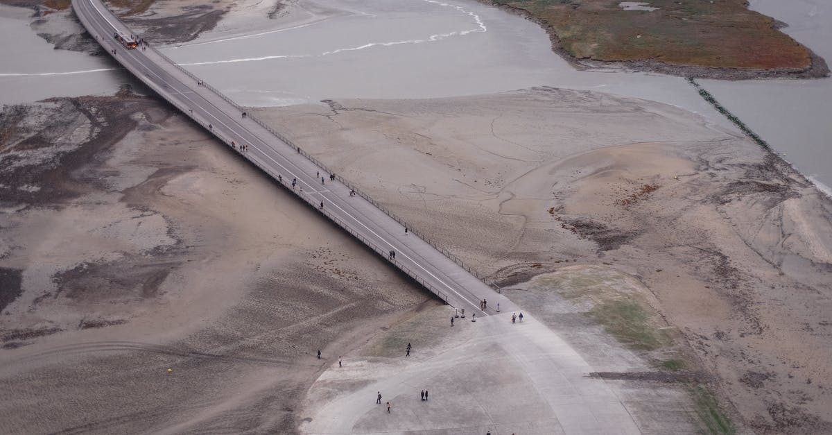 What is the best way to travel to the West Bank? - Drone view of road over river in barren valley What is the best way to travel to the West Bank? - Drone view of road over river in barren valley